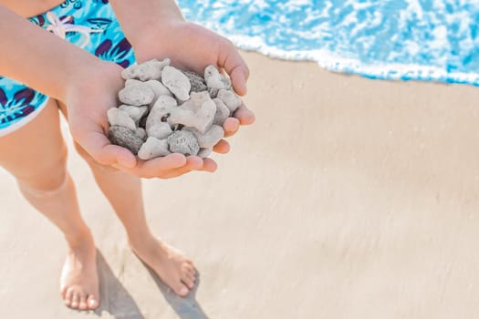 The hands of a young girl hold a pile of stones standing on the sea coast, copy the space.