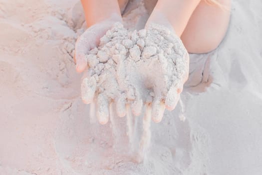 The hands of a young girl hold a pile of white sand close-up.