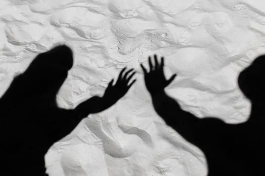 The black silhouette of a guy and a shadow girl stretched their arms forward on the white beach sand background.