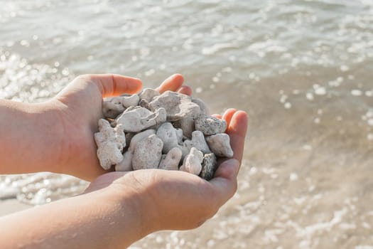 The girl's hands hold a pile of stones close up against the sea water.