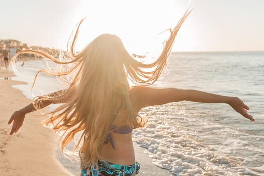 Young skinny girl throws up her hair and spreads her arms to the sides against the backdrop of the sea beach and sunset.