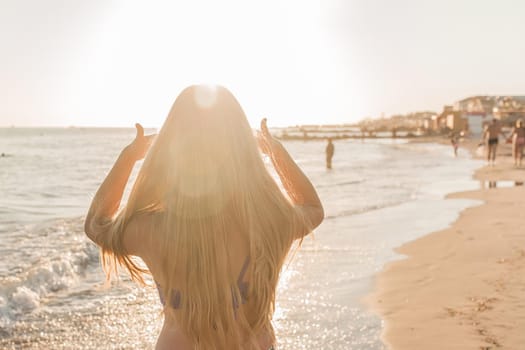 Young girl straightens her hair with her hands against the backdrop of the sea beach and sunset.