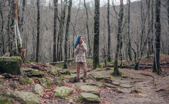 Beautiful young woman with blue hair wearing in sweater and cargo pants standing in the forest