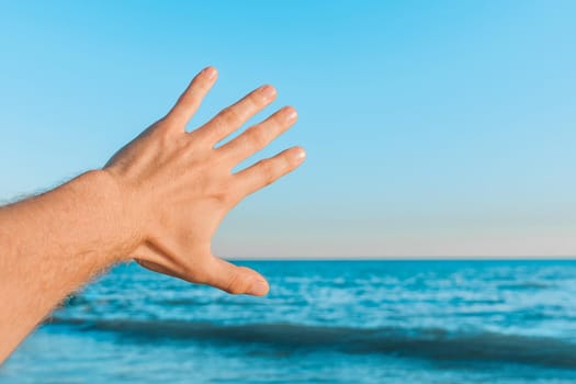 The guy's hand stretches or waves to the blue sea, the sky against the horizon line.