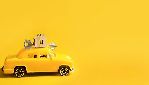 Yellow toy car with a key to the house on the roof on a color background. Moving to a new home, mortgage, buying an apartment, taxi. Copy space.