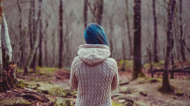 Young woman with blue hair walking in autumn forest, rear view