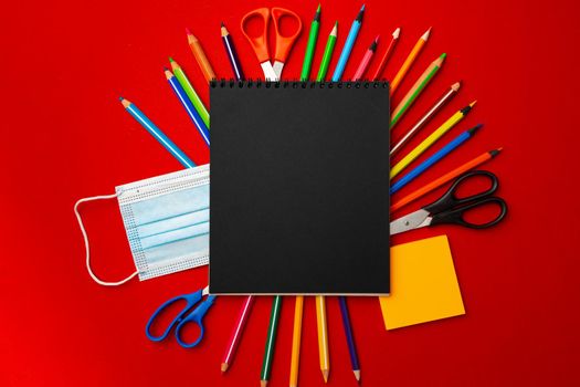 Black notepad page with stationery and medical mask on red background top view