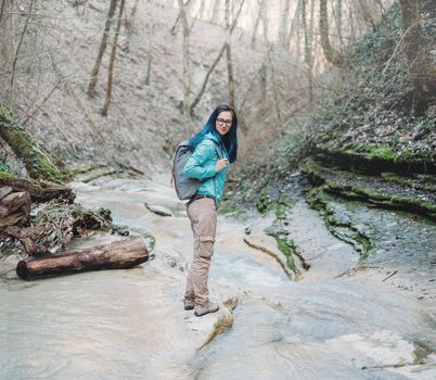 Hiker young woman with backpack crossing the mountain river in forest outdoor
