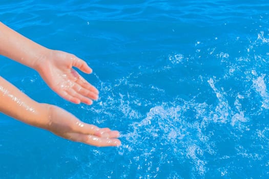 The hands of a young girl make splashes of blue pure sea water close-up.