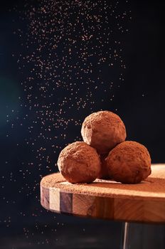 Homemade Chocolate Truffles with Sifting Cocoa on Wooden Board on Dark Background. Copy Space For Your Text.