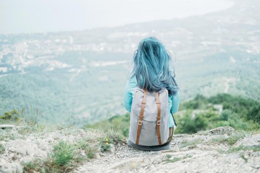 Traveler young woman with backpack resting on peak of mountain, rear view