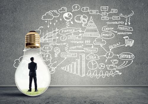 Businessman inside of light bulb in empty concrete room and sketches on wall