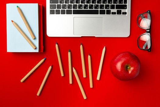 Top view of student working space with open laptop and red apple, other supplies