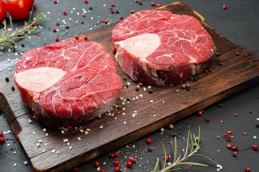 Two raw fresh marbled meat steak on dark background, cherry tomatoes and spices. Close up.