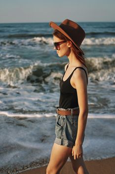 cheerful woman in sunglasses and a hat walks along the ocean. High quality photo
