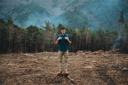 Traveler young man with backpack standing on tree stump in the forest outdoor