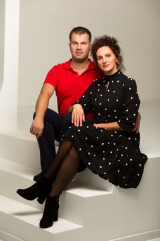 Beautiful family man and woman are sitting on the white stairs in the studio. The concept of love, friendship.