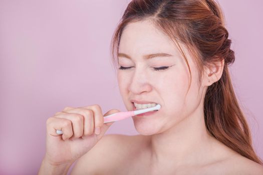 unhappy beautiful woman brushing her teeth on pink background