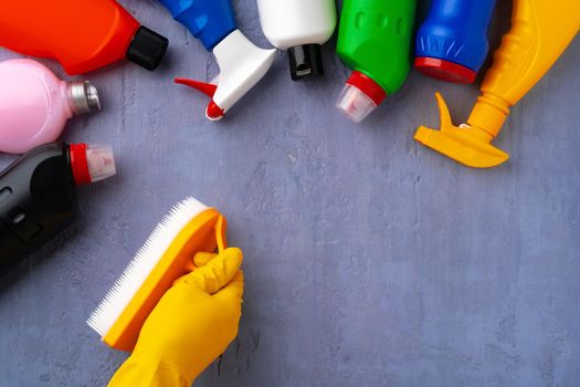 Cleaning supplies with hands in rubber gloves on gray background, top view