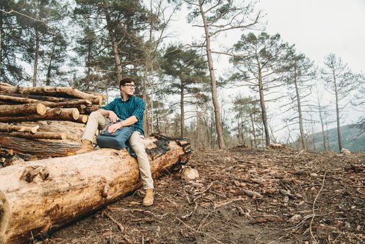 Hiker young man with backpack sitting on felled wood trunks in the forest outdoor