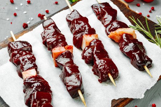 Raw liver kebab on skewers on wooden board close up
