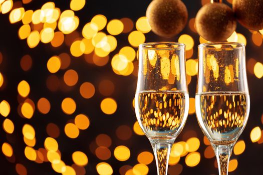 Two glasses of champagne and Christmas baubles on shiny bokeh lights background