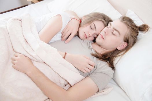 Close-up of a young couple in bed sleeping in an embrace, hiding behind a blanket. The concept of a young family and healthy sleep.