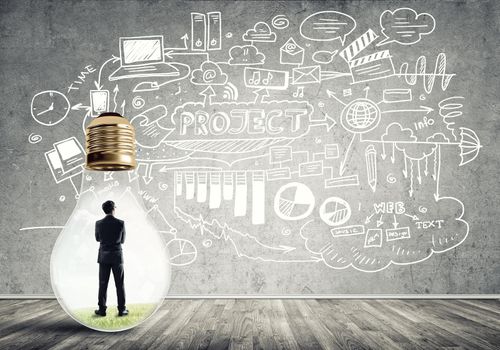 Businessman inside of light bulb in empty concrete room and sketches on wall