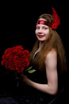 A beautiful teenage school girl is photographed in the studio with a large bouquet of flowers, against a black background.