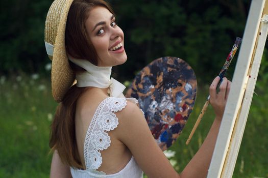 woman with a palette of paints painting a picture outdoors close-up. High quality photo