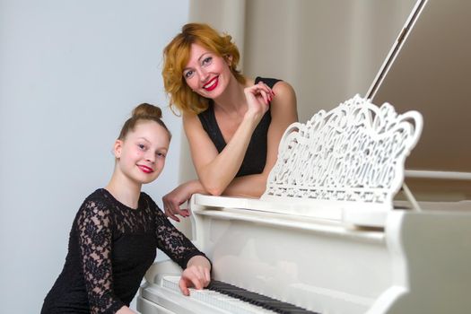 A beautiful young mother with a little daughter near a large white grand piano. The concept of family happiness, music education.