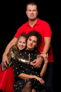 Family portrait, mom and dad with a charming little daughter. On a black background. The concept of family happiness.