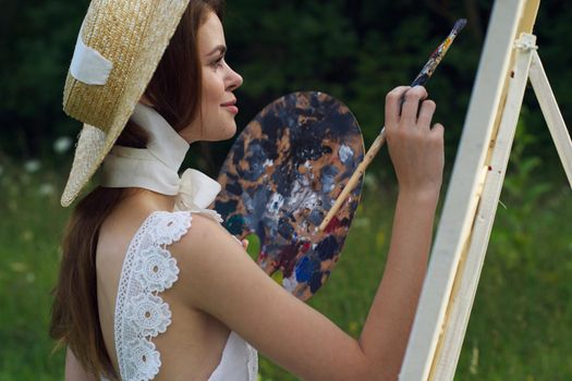 woman with a palette of paints painting a picture outdoors close-up. High quality photo