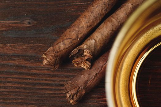 Glass of whiskey and rolled cigars on wooden table close up