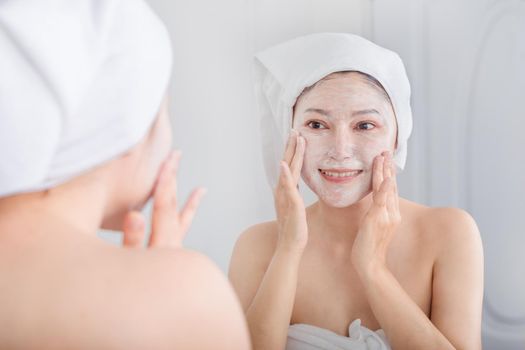 woman applying mask on her face and looking in the mirror in the bathroom