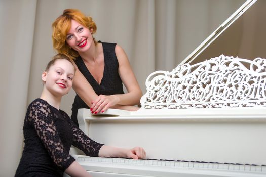 A beautiful young mother with a little daughter near a large white grand piano. The concept of family happiness, music education.