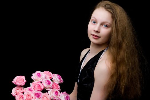 A beautiful teenage school girl is photographed in the studio with a large bouquet of flowers, against a black background.