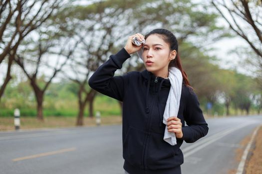 young sporty woman running and wiping her sweat with a towel in the park