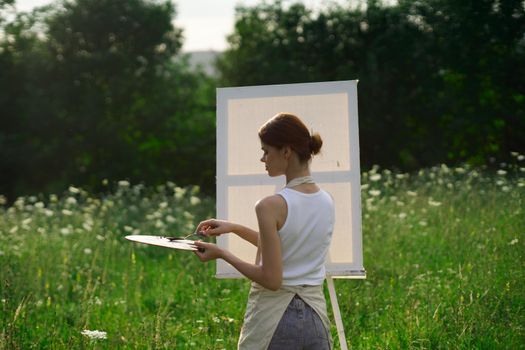 woman artist outdoors with palette of paints paints a picture. High quality photo