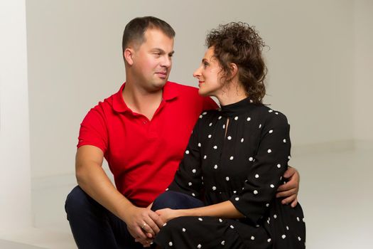 Beautiful family man and woman are sitting on the white stairs in the studio. The concept of love, friendship.