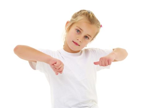 A beautiful little girl in an empty white T-shirt points to herself. The concept of design of T-shirts, advertising of children's goods. Isolated on white background.