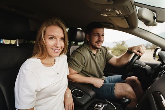 Beautiful young smiling couple sitting on front passenger seats and driving a car