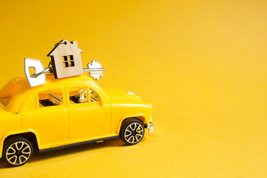 Yellow toy car with a key to the house on the roof on a color background. Moving to a new home, mortgage, buying an apartment, taxi. Copy space.
