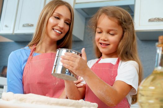 Mother and her little daughter preparing dough in kitchen close up