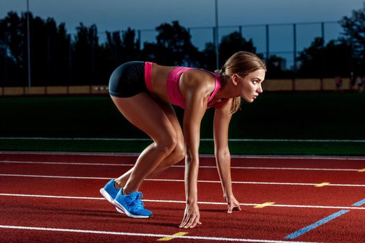 Portrait of beautiful woman ready to start running. Female athlete sprinter doing a fast sprint for competition on red lane at an outdoor field stadium.