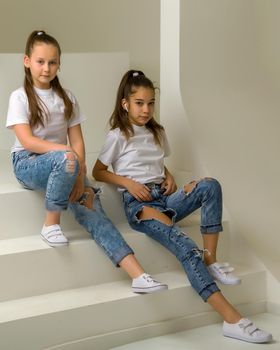 Smiling little girls are sitting on the white stairs in the studio.