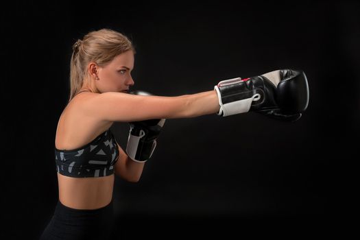Beautiful female athlete in boxing gloves, in the studio on a black background. The boxer fulfills the blow