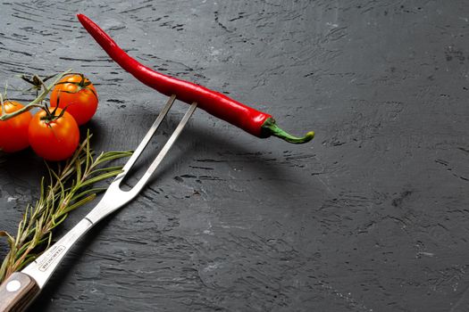 Red chili pepper on fork on black stone background close up