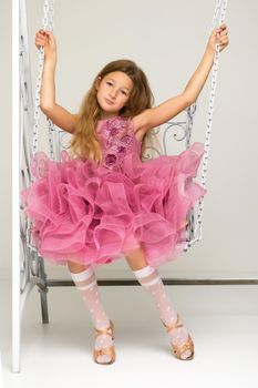 Beautiful little girl swinging in the studio on a swing. Concept of a happy childhood, family well-being.