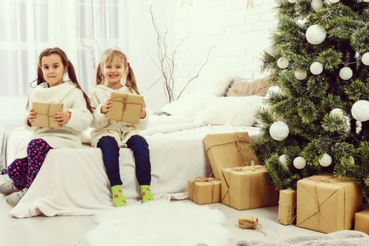 two girls in front of christmas tree with gifts and fire place